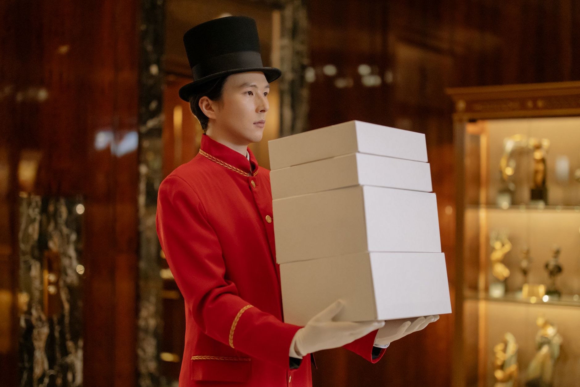 Asian hotel porter in red uniform indoors carrying multiple boxes with a profess