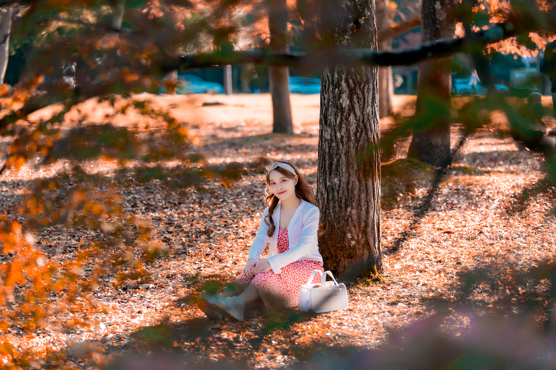 A woman sits joyfully under a tree amidst fallen autumn leaves, radiating warmth